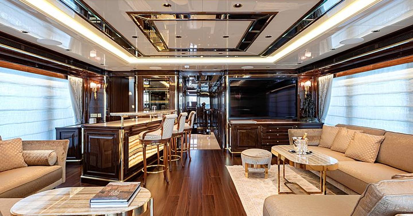 Long view of main salon onboard Sanlorenzo Lady Lena, sofas on either side with adjacent coffee tables, bar and stools in background