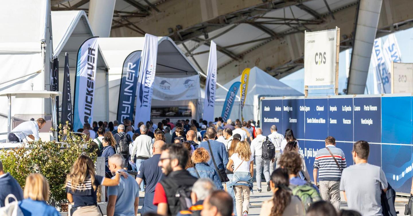 Visitors to the Genoa International Boat Show walking towards an entrance by exhibitor flags