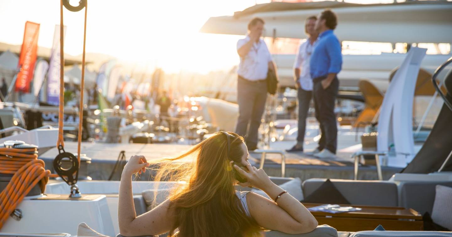 woman sits back on yacht on phone call with brokers on yacht next to her during palma superyacht show