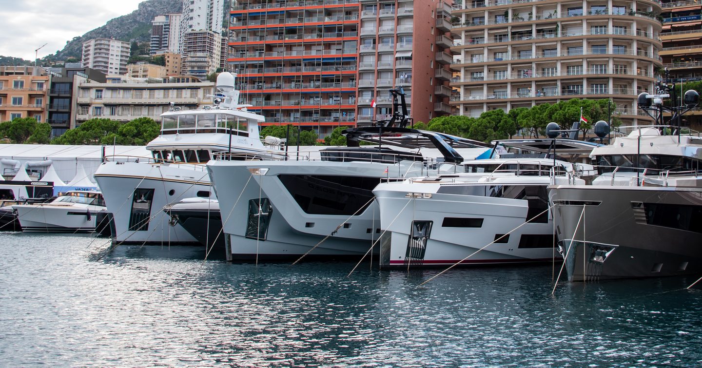 MYS 2024 shot of the bows of several motor yachts, with Monaco flats in background, grey day