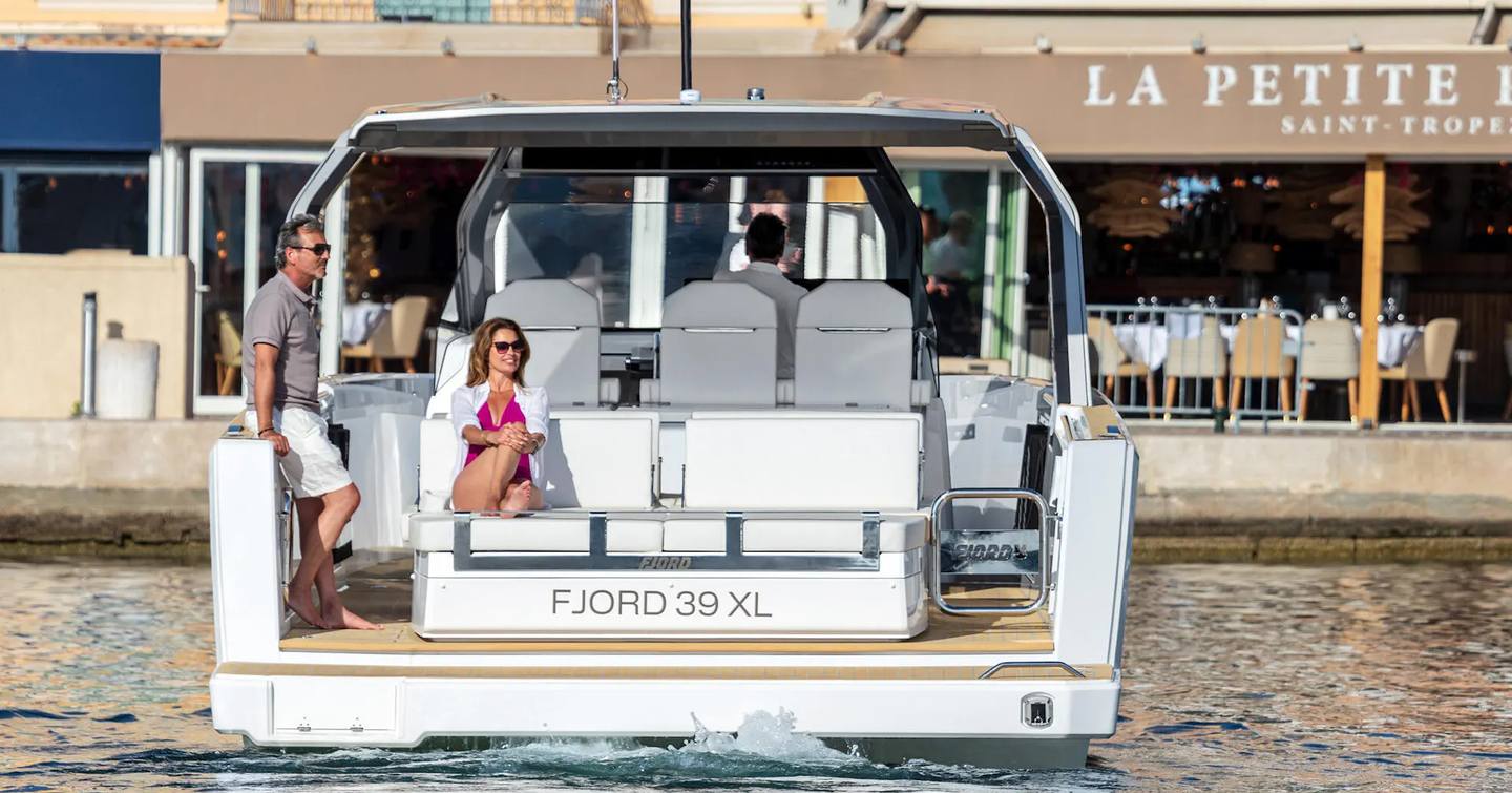 Fjord 39 XL shown aft deck woth two people onboard, the yacht is making way towards dock in what appears to be a French harbour