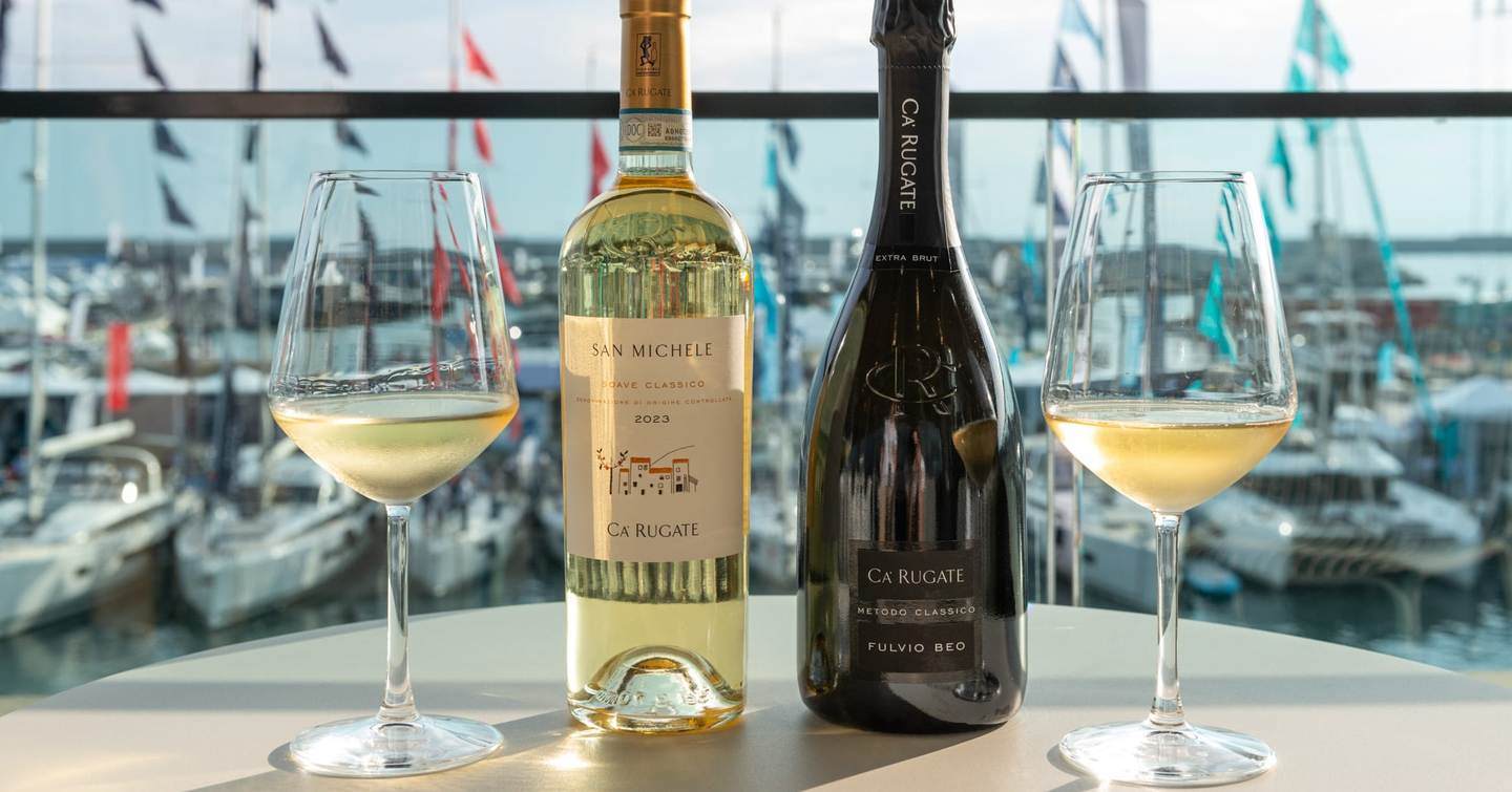 Two wine bottles and glasses on a table with boats visible in background