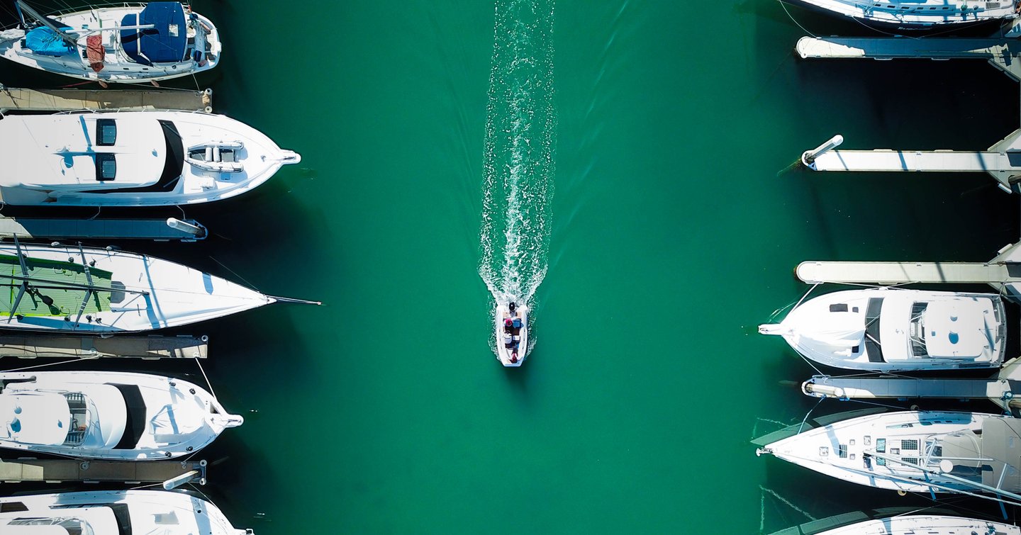 Tender boat traveling on water with row of yachts either side