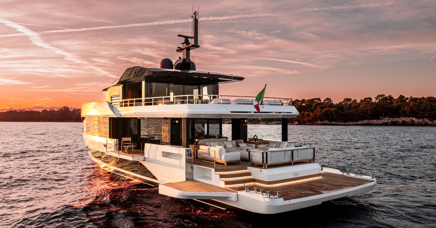 Arcadia A96 motor yacht shown at sunset, on anchor in still water with land in background; all side wings are open to extend the aft deck