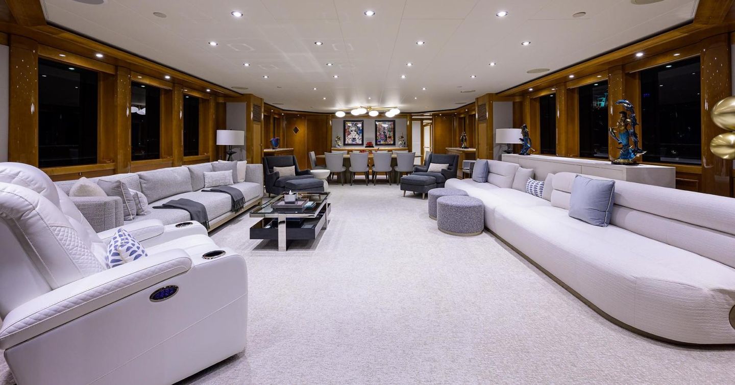 Overview of the main salon onboard the Quantum of Solace, white seating dotted around the walls facing in, with dining area in background.