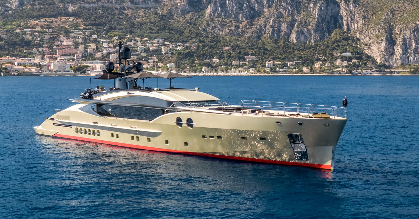 Side view of superyacht DB9 at sea, with cliffs in the background.