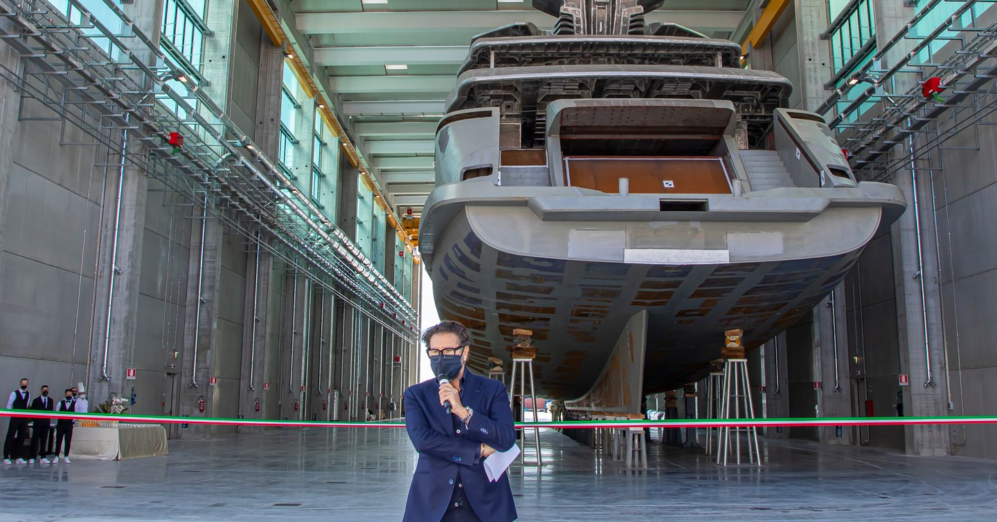 Man talking on microphone in front of ribbon and ship in background