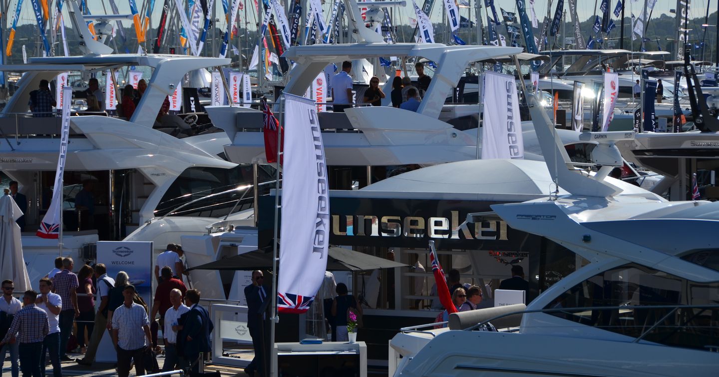 Crowds of people and yachts and Sunseeker sign on marquee at Southampton International Boat Show