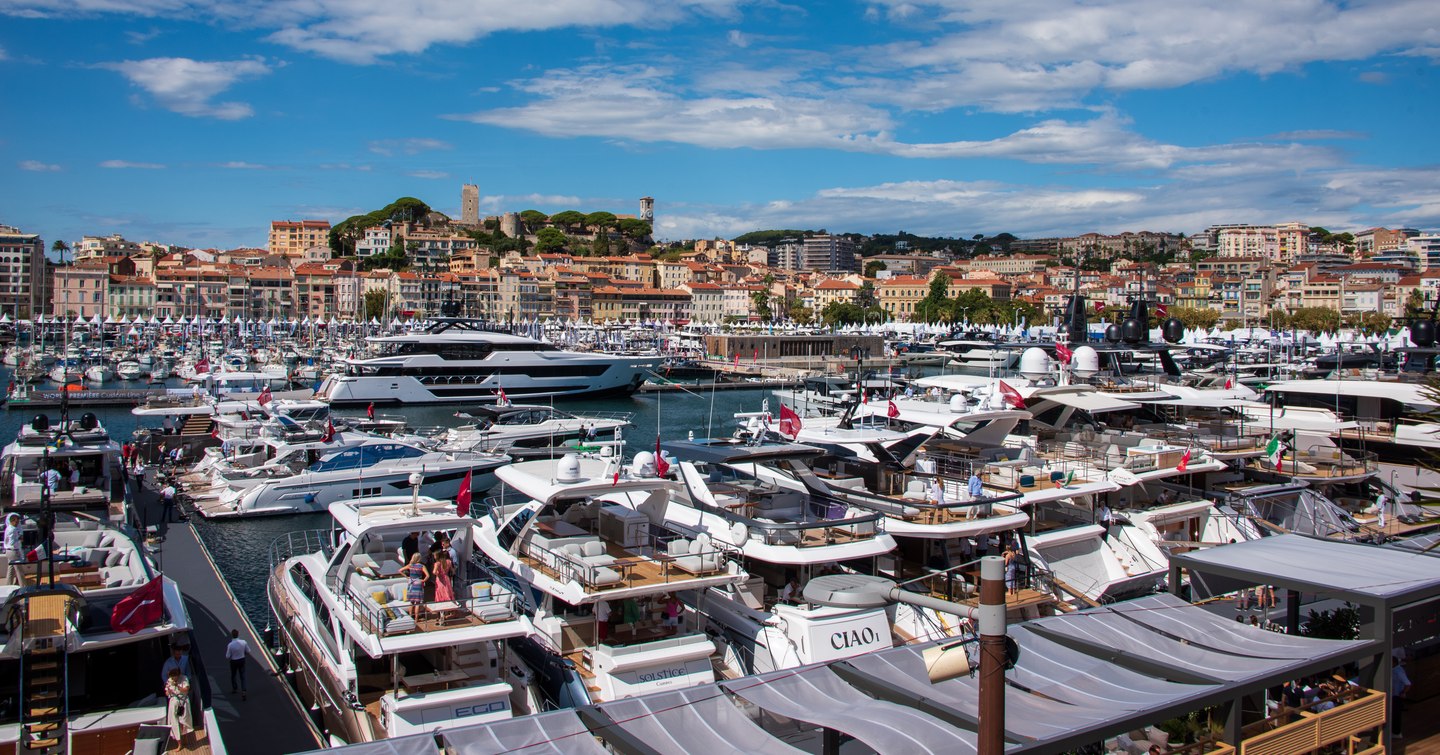 Overview of Vieux Port in Cannes. Many motor yachts berthed in marina with Cannes visible in background. 