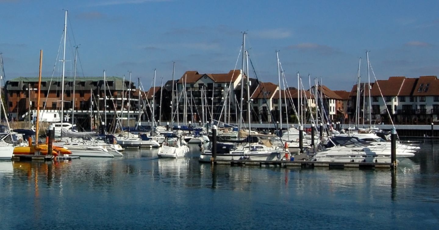 Water level view of Ocean Village Marina in Southampton. Many sailing boats berthed along pontoons with housing in the background.