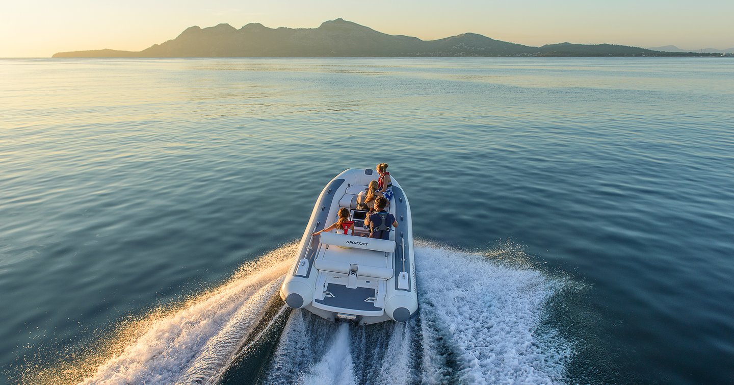 Williams SportJet 520 yacht tender running shot, mid aerial over aft of powerboat, fast as creating wake, land in background, smooth sea, bright early day