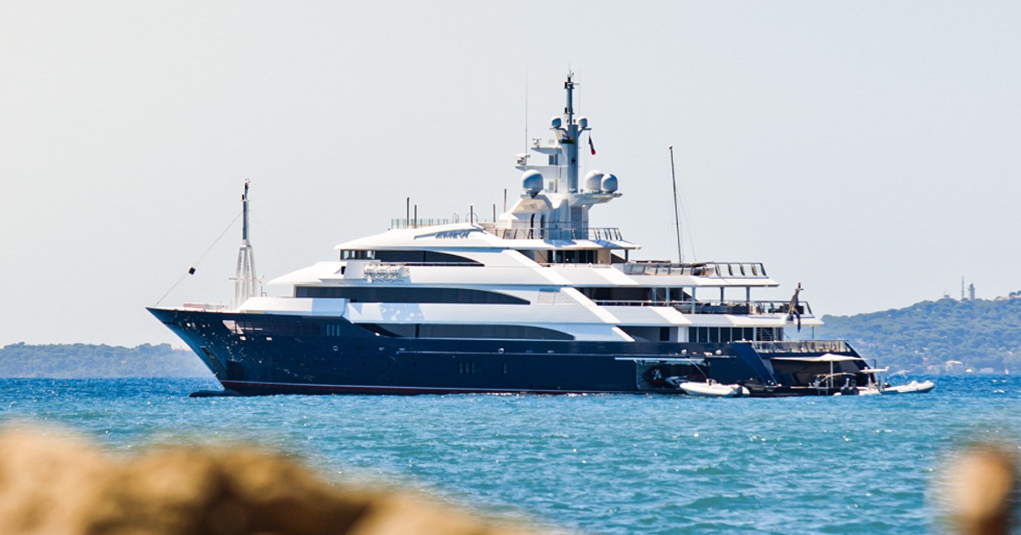 Oceanco yacht AALTO shown in far distance on anchor on bright day in calm sea, yacht's port side profile is shown