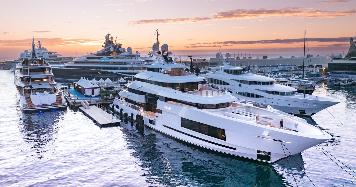 Superyachts berthed in Port Hercule, Monaco as the sun sets, creating a pink and purple sky