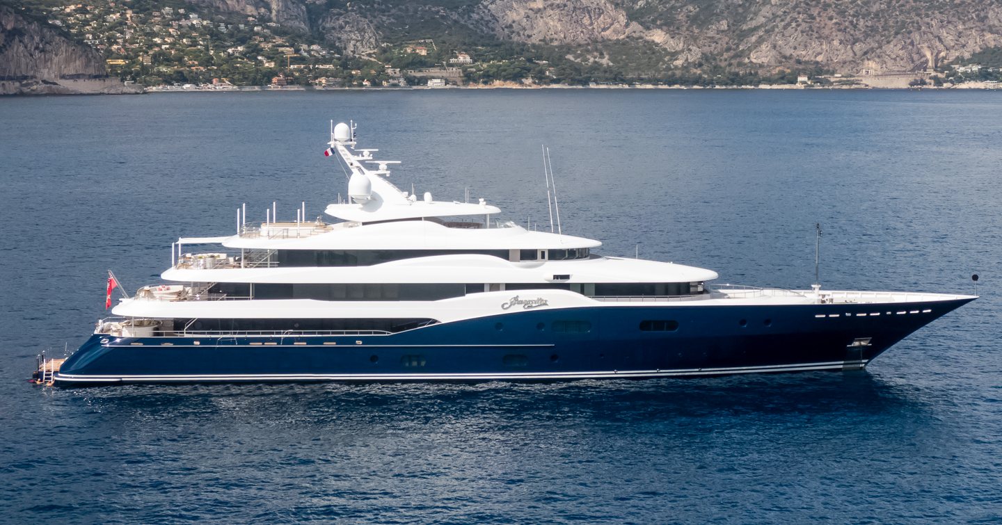 superyacht AMARYLLIS showing her blue hull and white superstructure in front of a mountainous backdrop