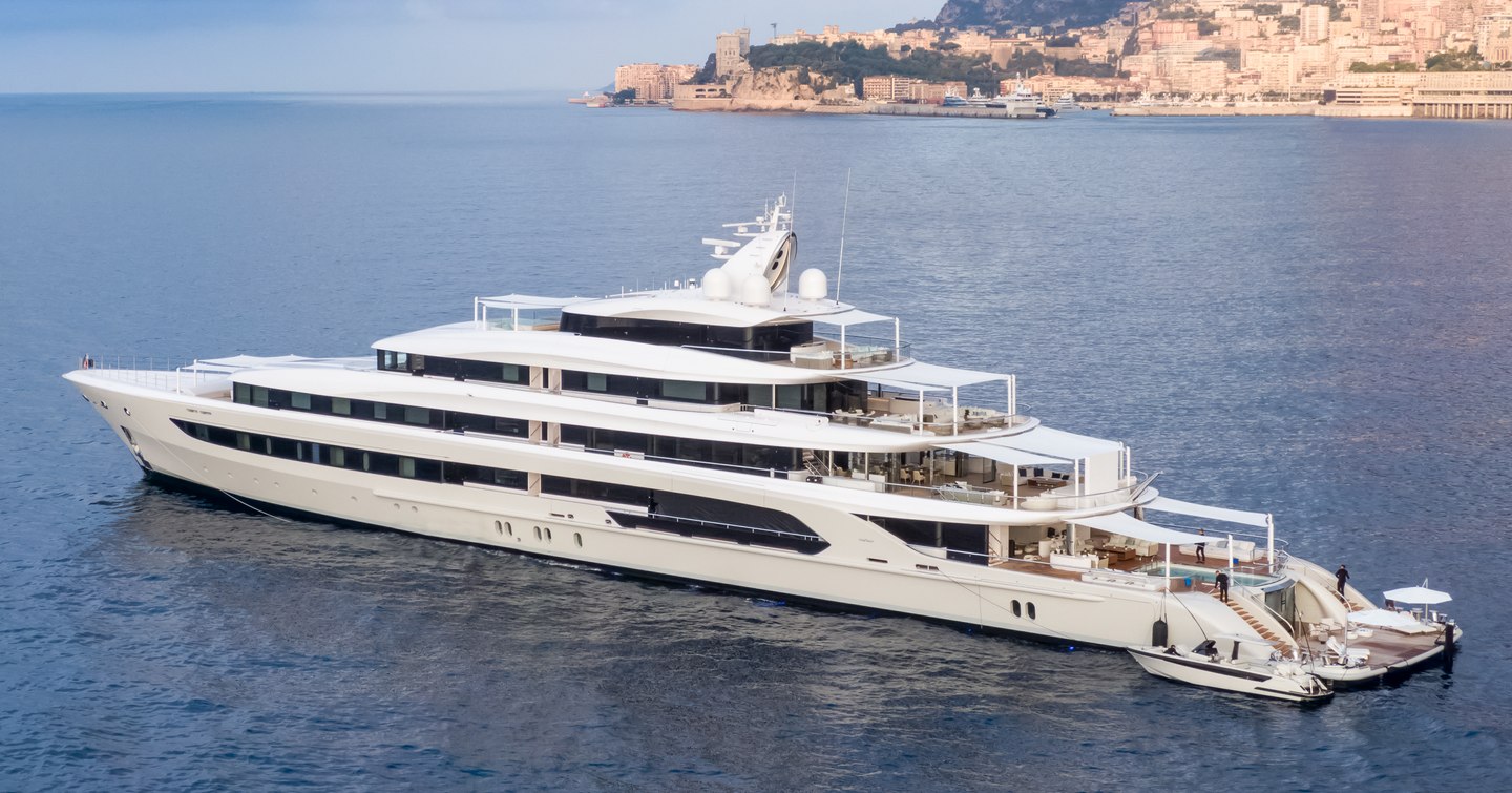 Oceanco yacht H3 shown on anchor in calm sea in bright day with land in background, port side profile showing