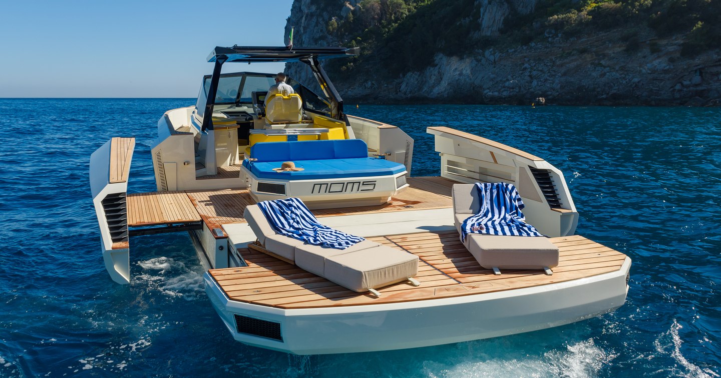 Aft view of Evo R4 XT anchored in a bay, with waterside terrace folded down and sun loungers on swim platform.