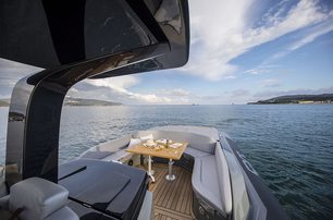 Sacs Tecnorib Strider 13 shot taken from onboard looking at the bow that has table set for dining, calm sea, bright sky approaching twilight, land to both sides but open view dead ahead