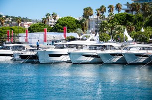 Cannes Yachting Festival shot with calm water in foreground and selection of motor boats in background with bows showing, red show flags in background, with trees