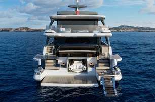 X100 Triplex by EXTRA Yachts shown above water level looking forward towards aft deck with bathing platform lowered and steps in to the water, calm water, bright day, tender shown in storage under transom