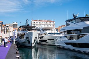 image taken at Cannes Yachting Festival with bright purple carpet on the dock on left hand side of image, and the bows of large motor boats facing the photographer, starboard side of motor yacht in right of image