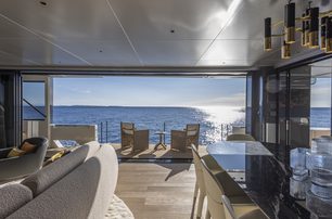 Arcadia A96 motor yacht interior salon looking out through large open glazing doors to the exterior seating area, sun low in sky casting reflection over water