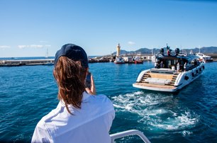 Cannes Yachting Festival the back of a lady in the foreground talking on VHF radio as small open motor cruiser leads the dock, in far distance you can see the lighthouse of Cannes