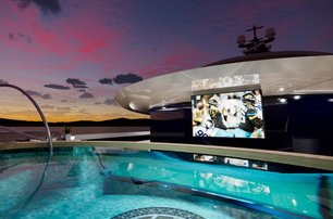 image shows the open air cinema onboard KISMET, shown at night time from the illuminated pool