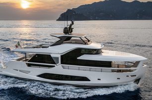 The Ferretti Yachts INFYNITO 80 making way at dusk through a flat sea with a rocky landscape in the background