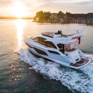 Manhattan 55 yacht mid aerial over port quarter deck and side profile, sun setting in background, land in background, slight wake indicates yacht moving at speed