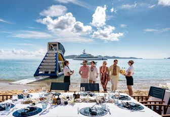 hospitality crew with guests at beach picnic superyacht background