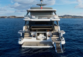 X100 Triplex by EXTRA Yachts shown above water level looking forward towards aft deck with bathing platform lowered and steps in to the water, calm water, bright day, tender shown in storage under transom