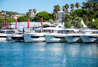 Cannes Yachting Festival shot with calm water in foreground and selection of motor boats in background with bows showing, red show flags in background, with trees