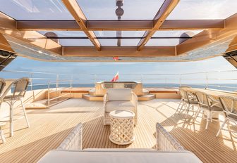 100 Sunreef Power exterior deck shot taken from inside, looking out over freestanding furniture over a mirror like sea, on a very bright day, the light coming through the roof panels casting shadows on the smart teak deck