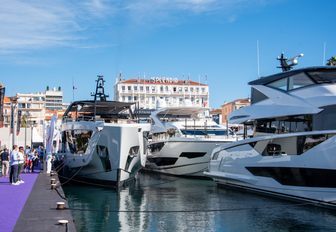 image taken at Cannes Yachting Festival with bright purple carpet on the dock on left hand side of image, and the bows of large motor boats facing the photographer, starboard side of motor yacht in right of image