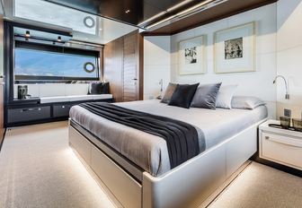 rendering of a large bed with white linen and a black runner, white wall panels and a white carpet in the master suite on board the Argo 90 yacht