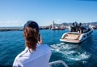 Cannes Yachting Festival the back of a lady in the foreground talking on VHF radio as small open motor cruiser leads the dock, in far distance you can see the lighthouse of Cannes