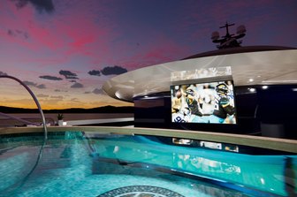 image shows the open air cinema onboard KISMET, shown at night time from the illuminated pool