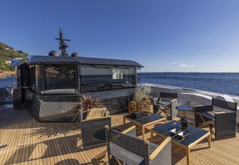 Arcadia A96 motor yacht upper deck as sun starts to set, free standing furniture show plenty of seating, smooth sea in background, shot taken from back of aft deck