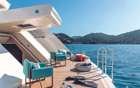 Beach club environment onboard CRN RIO superyacht. Side view with teal armchairs and water sports equipment visible.