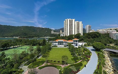 Exterior view of Lantau Yacht Club clubhouse, surrounded by green foliage and towering skyscrapers in background.