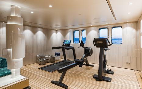 Overview of gym onboard superyacht SOARING. Row of gym equipment facing small windows looking over the sea.