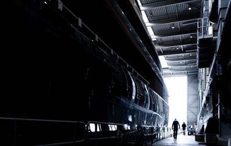 Ground level view of the Feadship Project 710 hull inside the construction shed prior to transit. With a couple of crew members walking alongside.