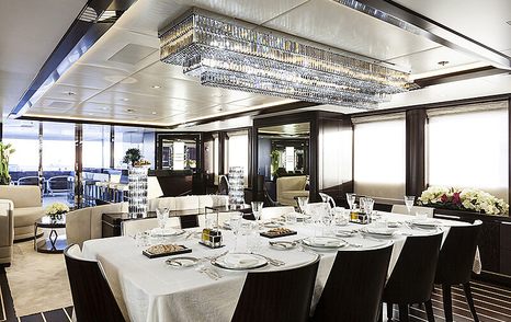 Main salon onboard the M/Y JULIA. Formal dining area in foreground with lounge visible in background, surrounded by large windows.