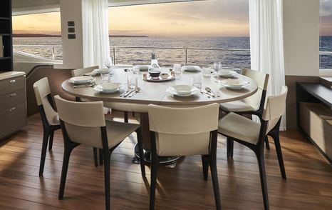 Dining area onboard Princess Y85. Circular table surrounded by chairs for eight guests, large windows surround.