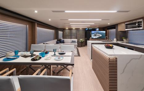 Dining area onboard Horizon FD75, dining table with four chairs to port side, with galley on starboard, overlooking lounge area in background.