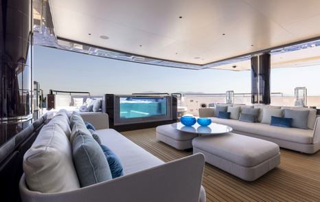 Aft deck onboard Superyacht POLESTAR, sofas facing inwards towards each other with a coffee table centre, pool visible towards aft of deck.