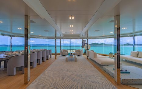 Overview of upper salon onboard superyacht WANDERLUST. Dining setup to port side with bountiful cream coloured seating to starboard.