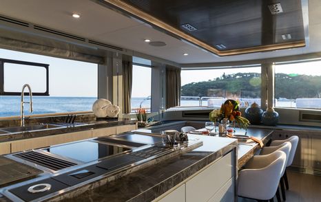 Galley onboard Sirena 78, large island in centre with counters behind and dining area adjacent.