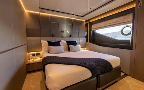 Guest cabin onboard Sunseeker 100 Yacht, central berth with nightstand either side plus oblong window to starboard.