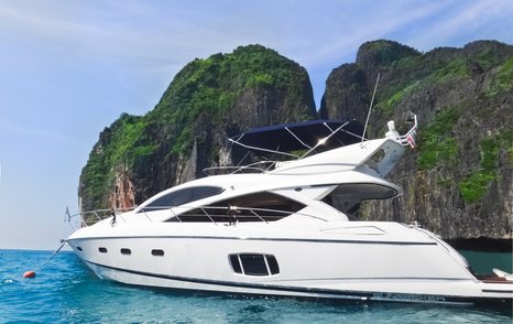 Motoryacht at anchor beside Hong Island, tall cliffs and rock formation in background, surrounded by sea